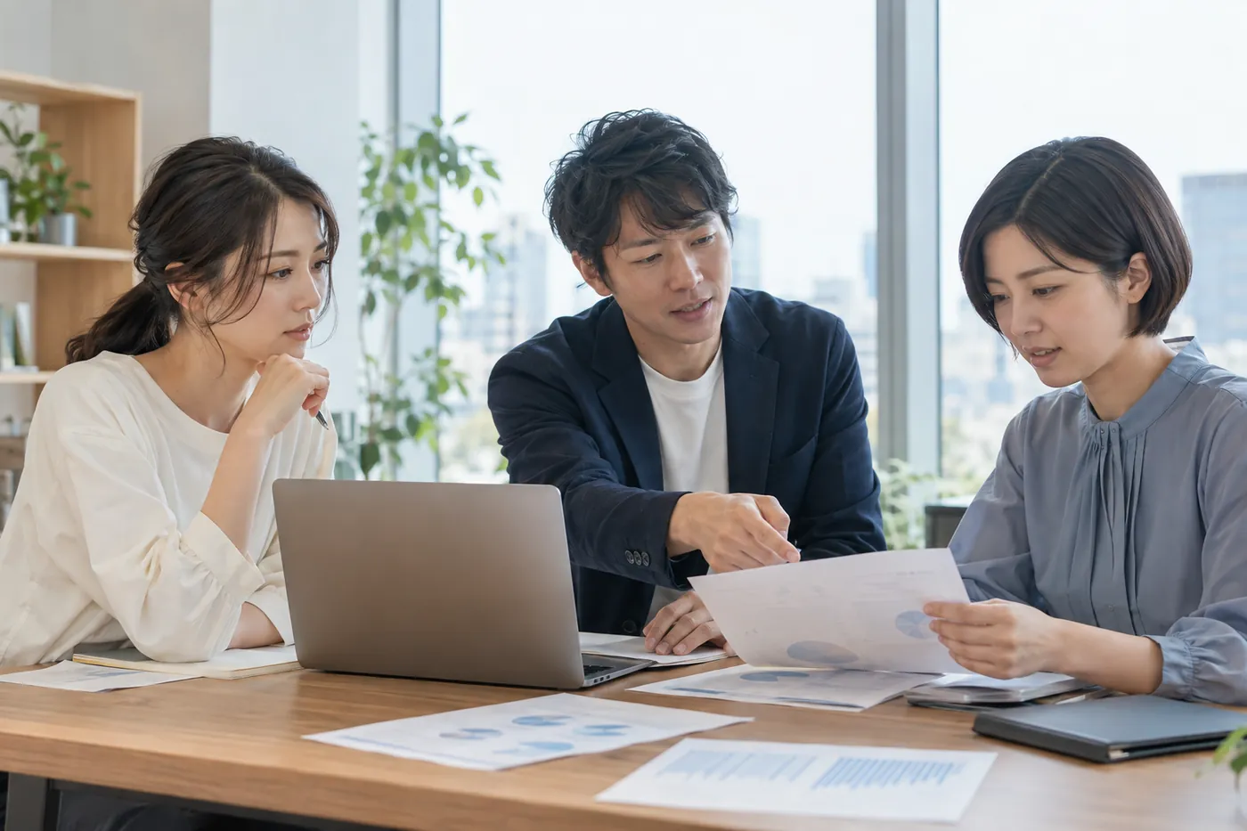 事務所で資料を囲んで打ち合わせをする所員 3 名